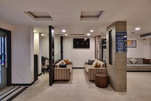 A modern lobby with striped sofas, a reception desk, and directional signage for amenities like the restaurant, business center, banquet, and summit hall. - Click Hotel Yuvraj (Surat)