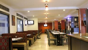 A restaurant with booths and tables, a TV screen, and a counter. - Click Hotel Yuvraj (Surat)