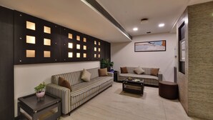A modern living room with striped sofas, a coffee table, and a decorative wall panel with recessed lighting. - Click Hotel Yuvraj (Surat)