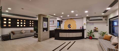 A modern reception area with a reception desk, sofas, and potted plants.