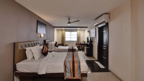 A hotel room with two beds, a ceiling fan, an air conditioning unit, a desk, and a television. - Click Hotel Yuvraj (Surat)