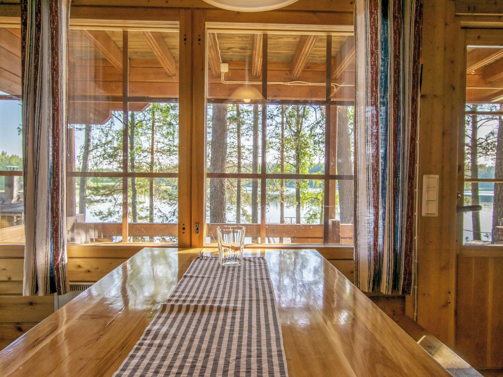 Un interior de madera con ventanas amplias, un mantel a cuadros y una silla.