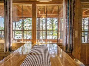 Un intérieur en bois avec de grandes fenêtres, un chemin de table à carreaux et une chaise.