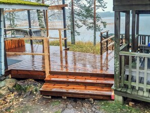 A wooden deck with steps leading to a covered area, surrounded by trees and a body of water.