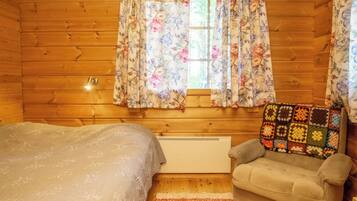 Ein gemütliches Cabin-Zimmer mit einem Bett, einem Sessel, einem Fenster mit floralen Vorhängen und einer Heizung.