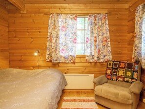 Acogedora habitación tipo cabaña con una cama, un sillón, una ventana con cortinas florales y un radiador.