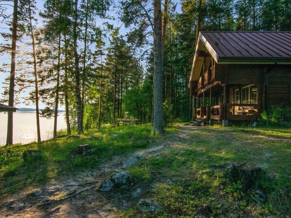 A cabin with a porch, surrounded by trees and a body of water.