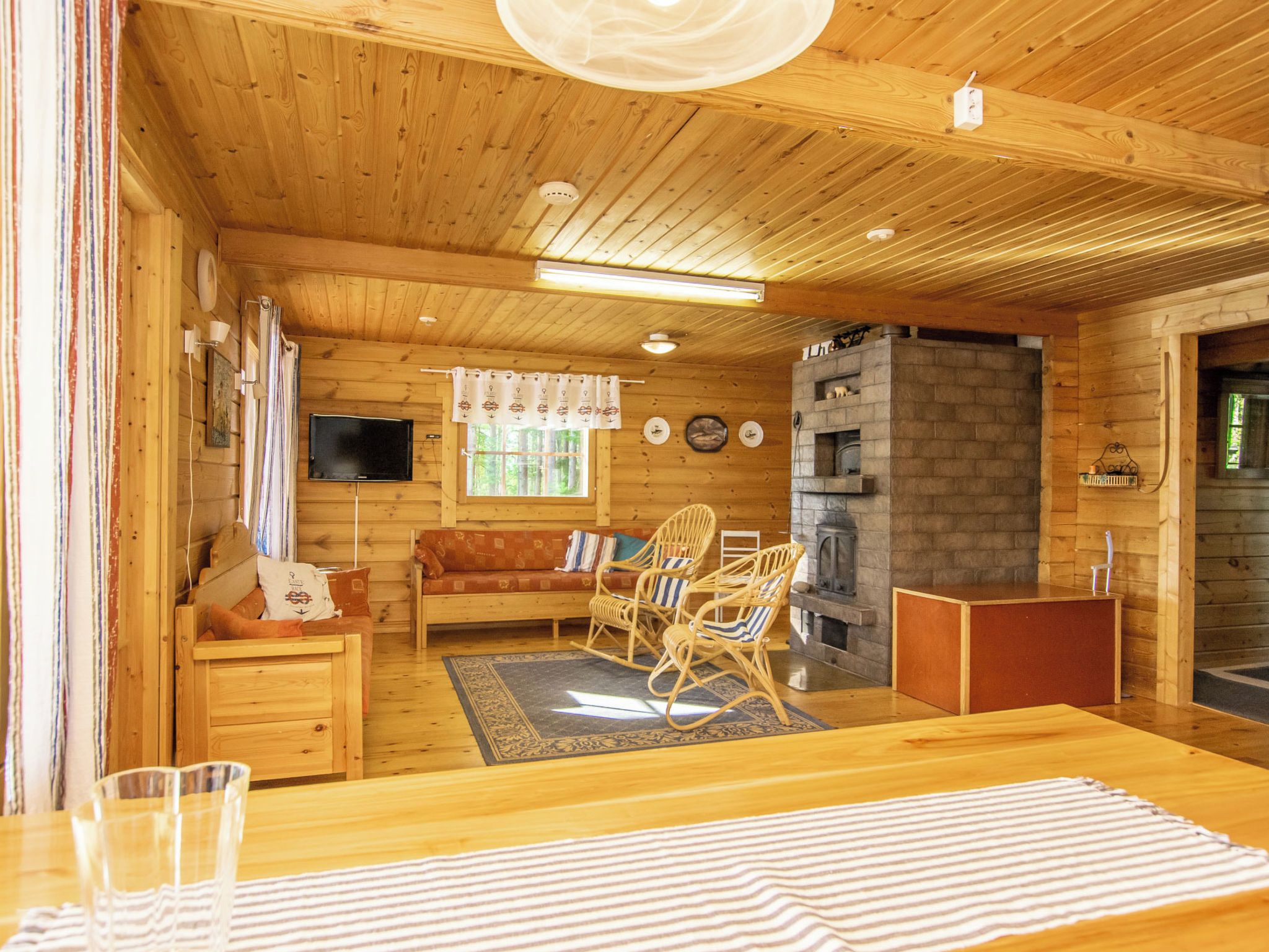 Ein gemütliches Blockhaus-Interieur mit Holzbalkendecke, Kamin, einer Couch und einem Essbereich.