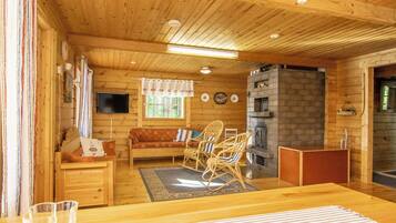Ein gemütliches Blockhaus-Interieur mit Holzbalkendecke, Kamin, einer Couch und einem Essbereich.