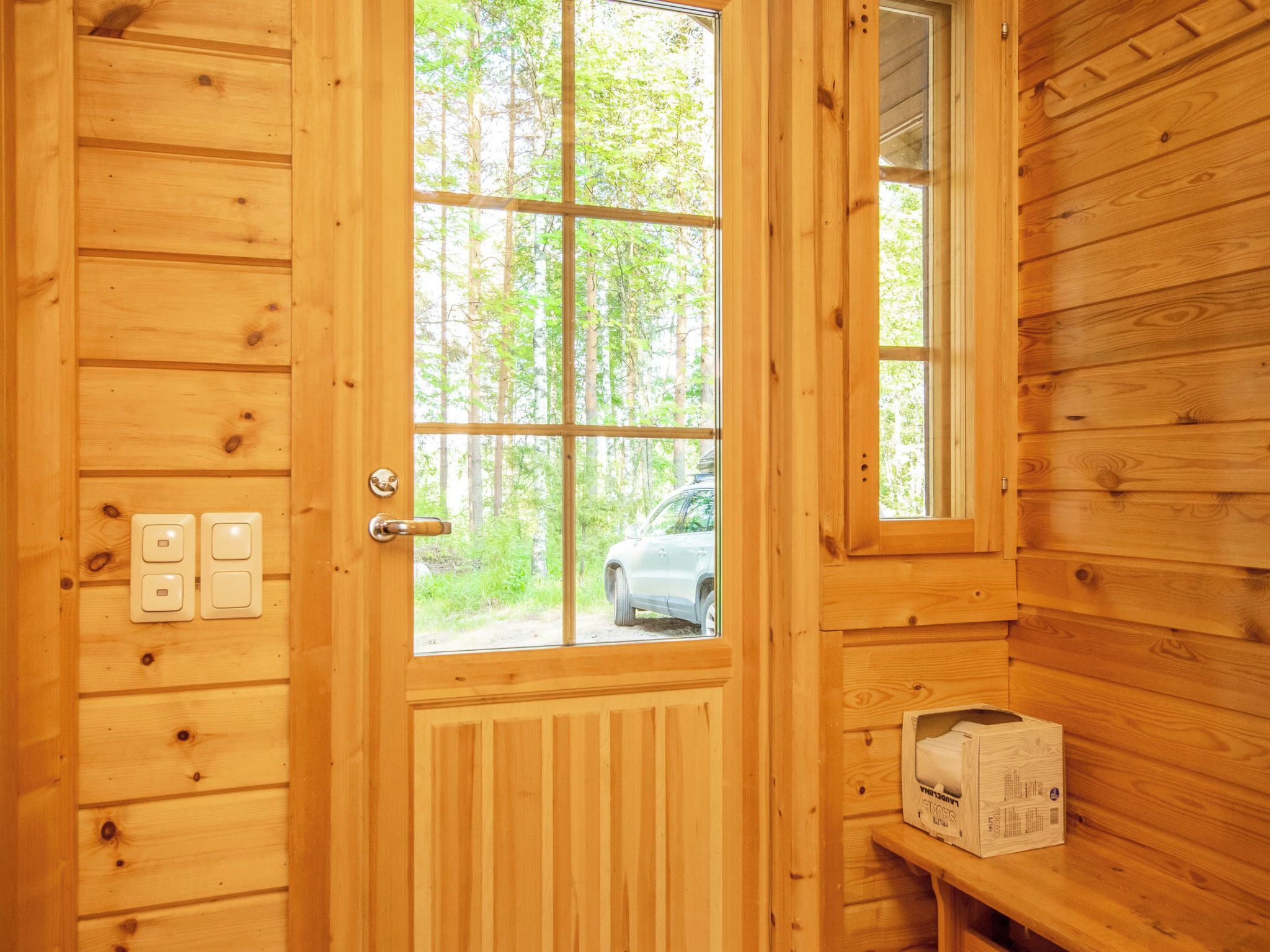 Eine Holztür mit Fenster, ein geparktes Auto davor und eine Kiste auf einem Regal.