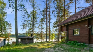 A cabin with a wooden exterior, a porch, and a view of a lake surrounded by tall trees. - Vacation home Utras by Interhome (Savonlinna)