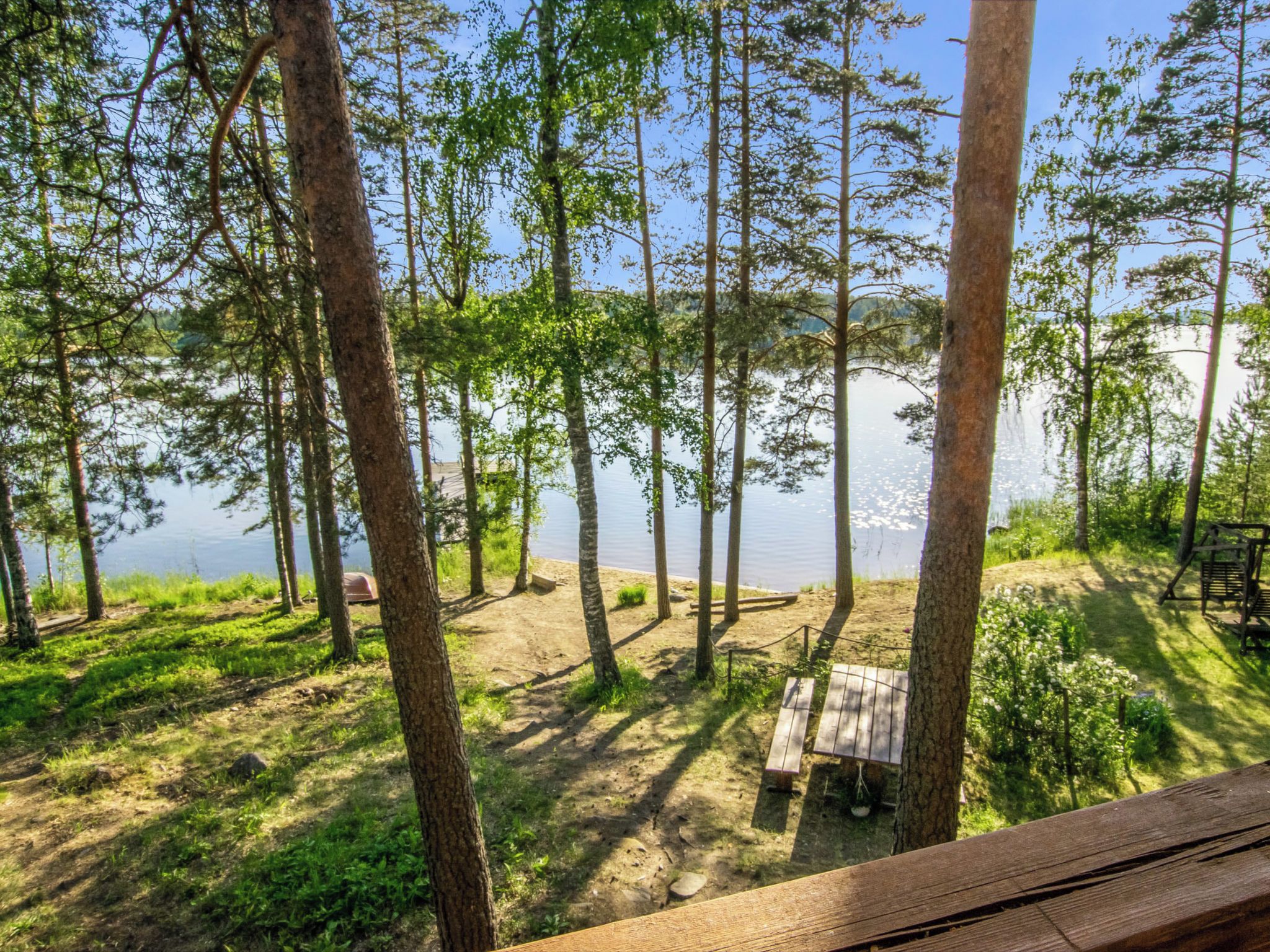 Metsäinen alue, jossa on puinen terassi ja penkki, jolta avautuu näkymä vesistöön.
