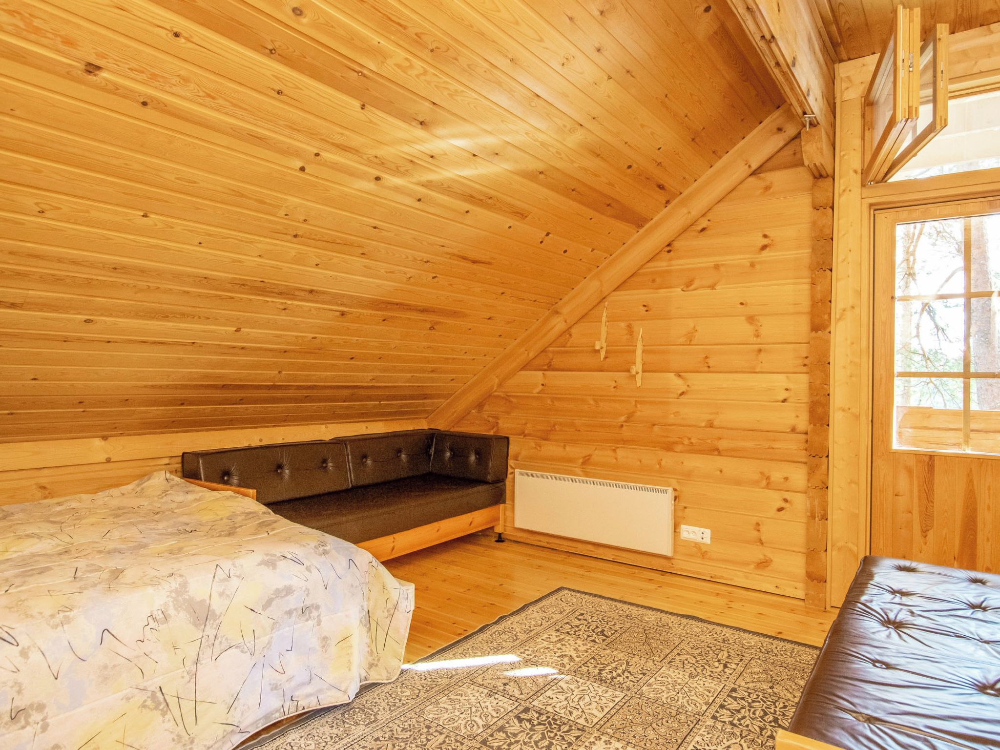 Ein Zimmer einer Holzhütte mit einem Bett, einer Bank und einem Fenster.