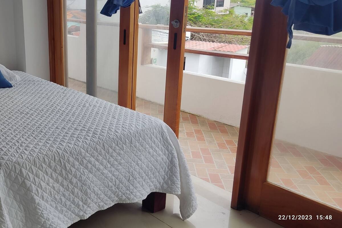 Une chambre avec un lit, une table de chevet, une lampe et une vue sur le balcon extérieur.