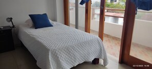 Ein Schlafzimmer mit Bett, Nachttisch, Lampe und Blick auf den Balkon.