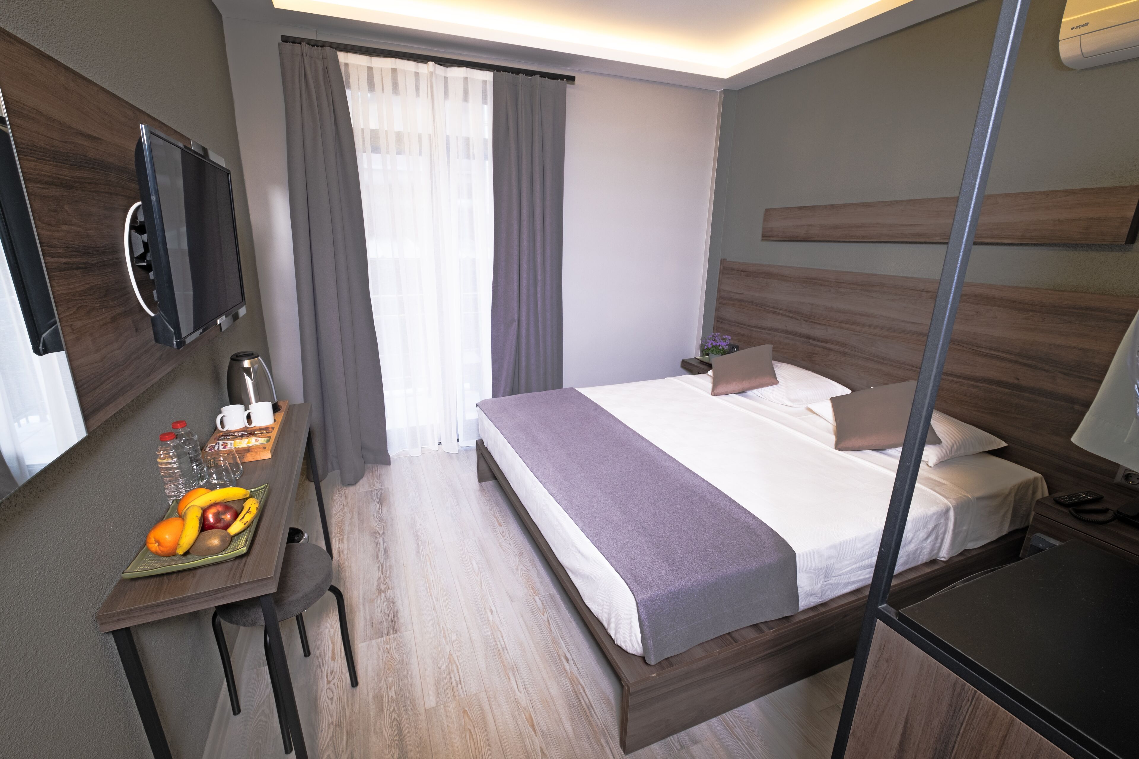 Une chambre d’hôtel avec un lit, une table de chevet, une télévision et un bureau avec des fruits et une tasse.