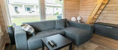 Ein modernes Wohnzimmer mit einem grauen Ecksofa, einem kleinen schwarzen Couchtisch und einem großen Fenster mit Blick nach draußen.