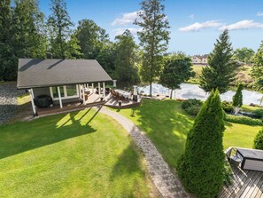 Ein Haus mit einer Terrasse, einem Teich und einem gepflegten Rasen.