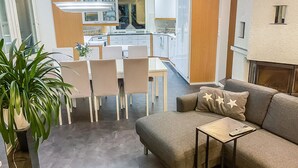A modern living room with a grey sofa, a coffee table, and a dining area with a white table and chairs.