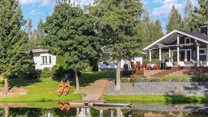 A lakeside property with a dock, kayaks, a covered patio, and a white house in the background.