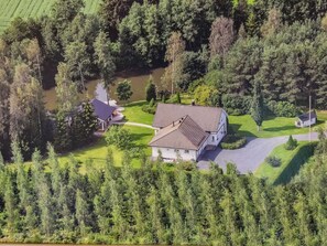 Ein großes Haus mit Schrägdach, umgeben von dichtem Wald und einem kleinen Teich.