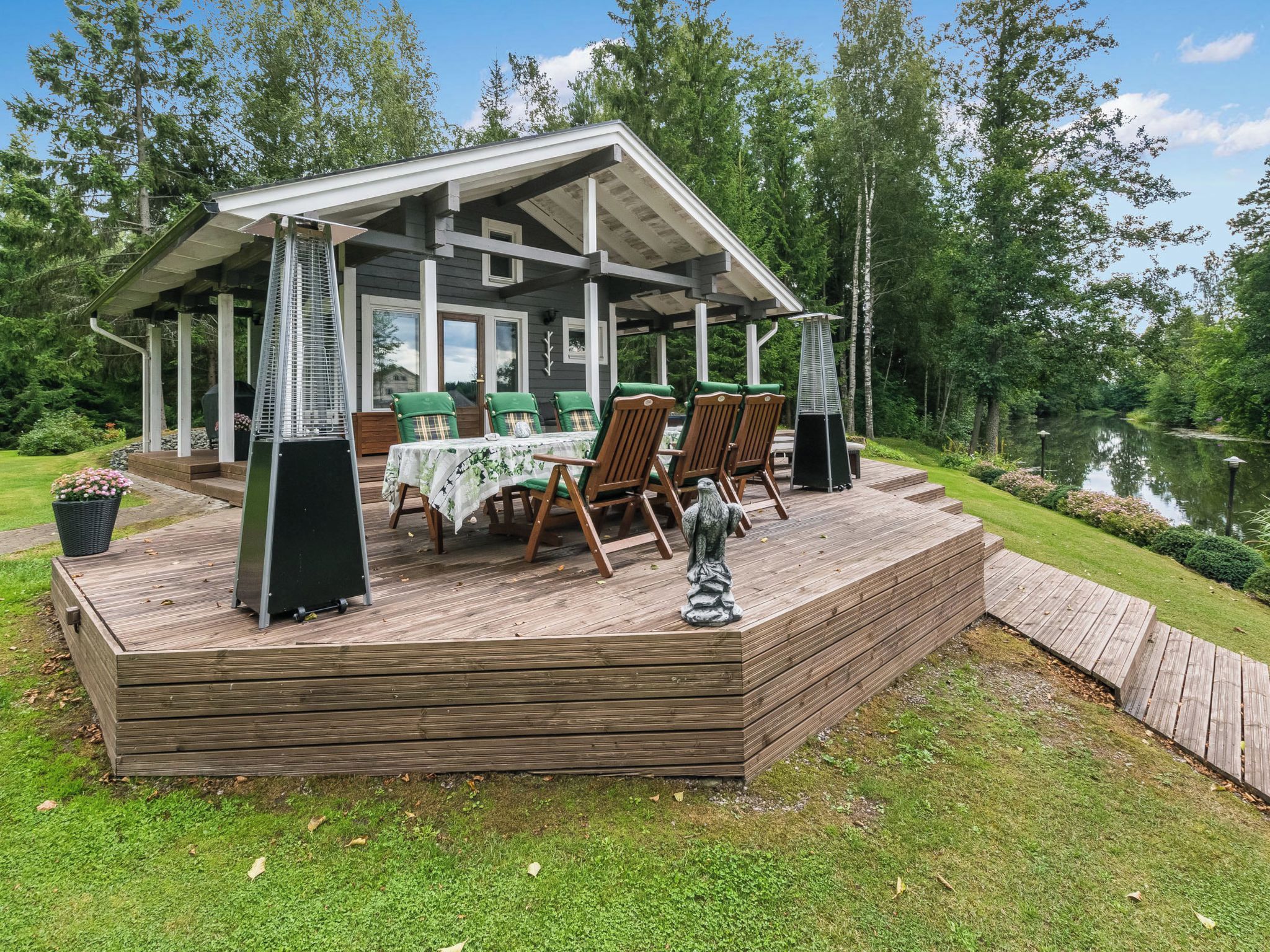 Un espace extérieur abrité, doté d’une table et de chaises, entouré d’une terrasse en bois et bordé par un plan d’eau.