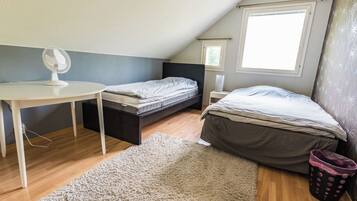 A small, well-lit attic bedroom with a desk, two beds, a large window, and a ceiling fan.