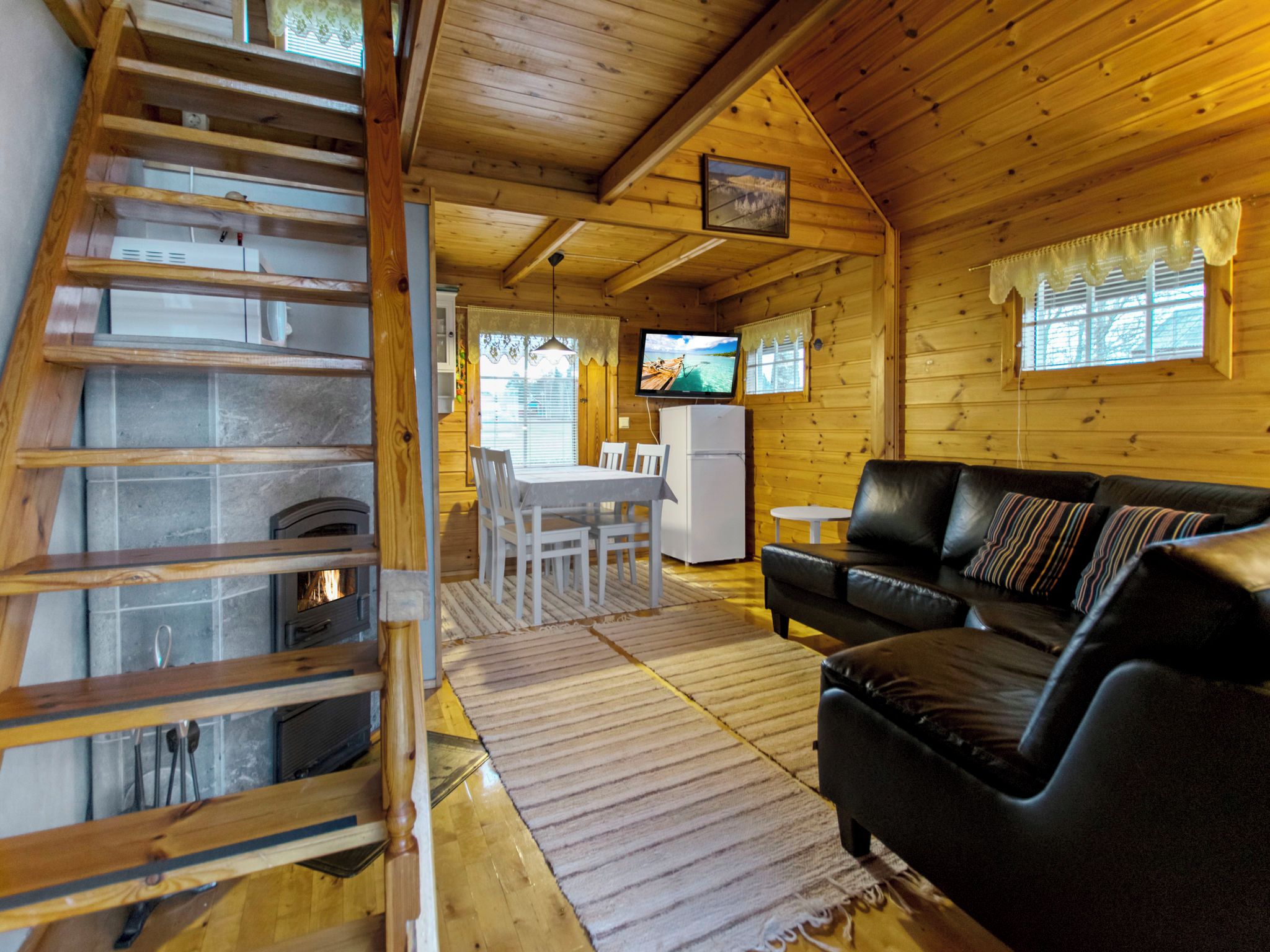 Interior d'una cabana de fusta amb zona de menjador, un sofà de pell negra, una televisió i una llar de foc.