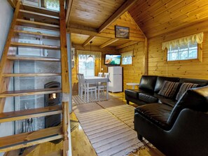 A wooden cabin interior with a dining area, a black leather sofa, a television, and a fireplace.