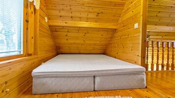 Pieni, puinen mökkihuone, jossa on lattialla patja, vasemmalla ikkuna ja oikealla puinen kaide.