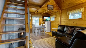 A cozy cabin interior with a wooden staircase, a dining area, a living room with a leather sofa, and a television.