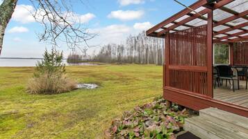 A wooden deck with a covered seating area overlooking a grassy field and a body of water.