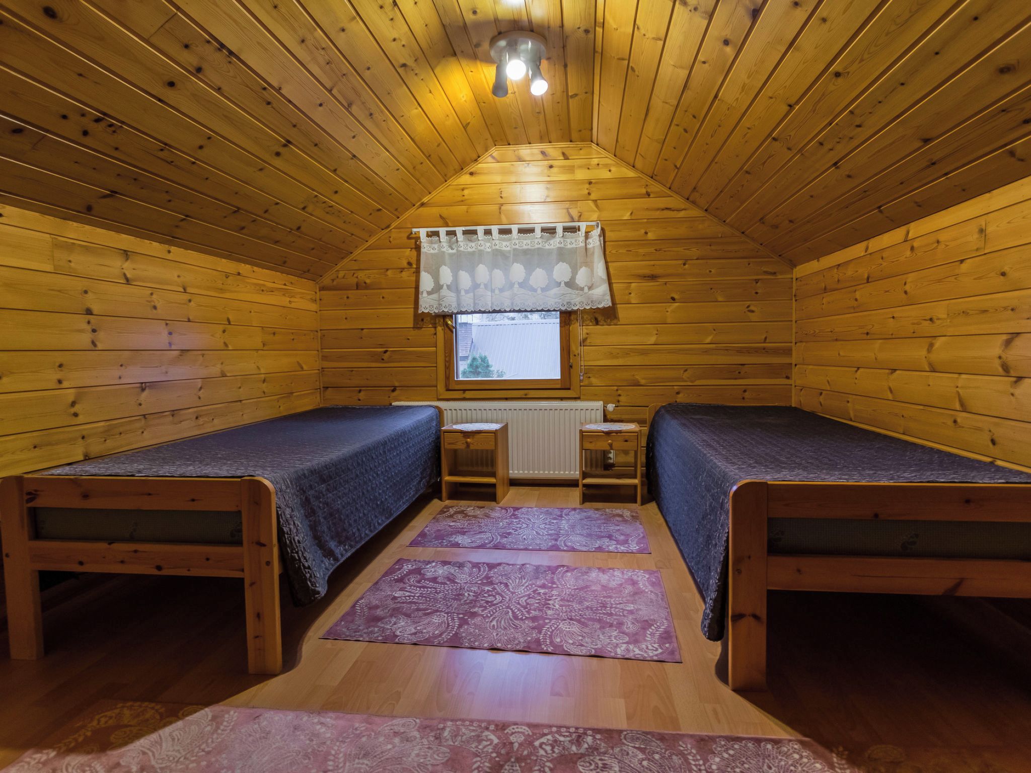 A small, wooden cabin with two single beds, a window with a curtain, and a ceiling light.