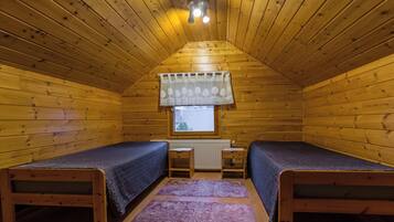 A small, wooden cabin with two single beds, a window with a curtain, and a ceiling light.