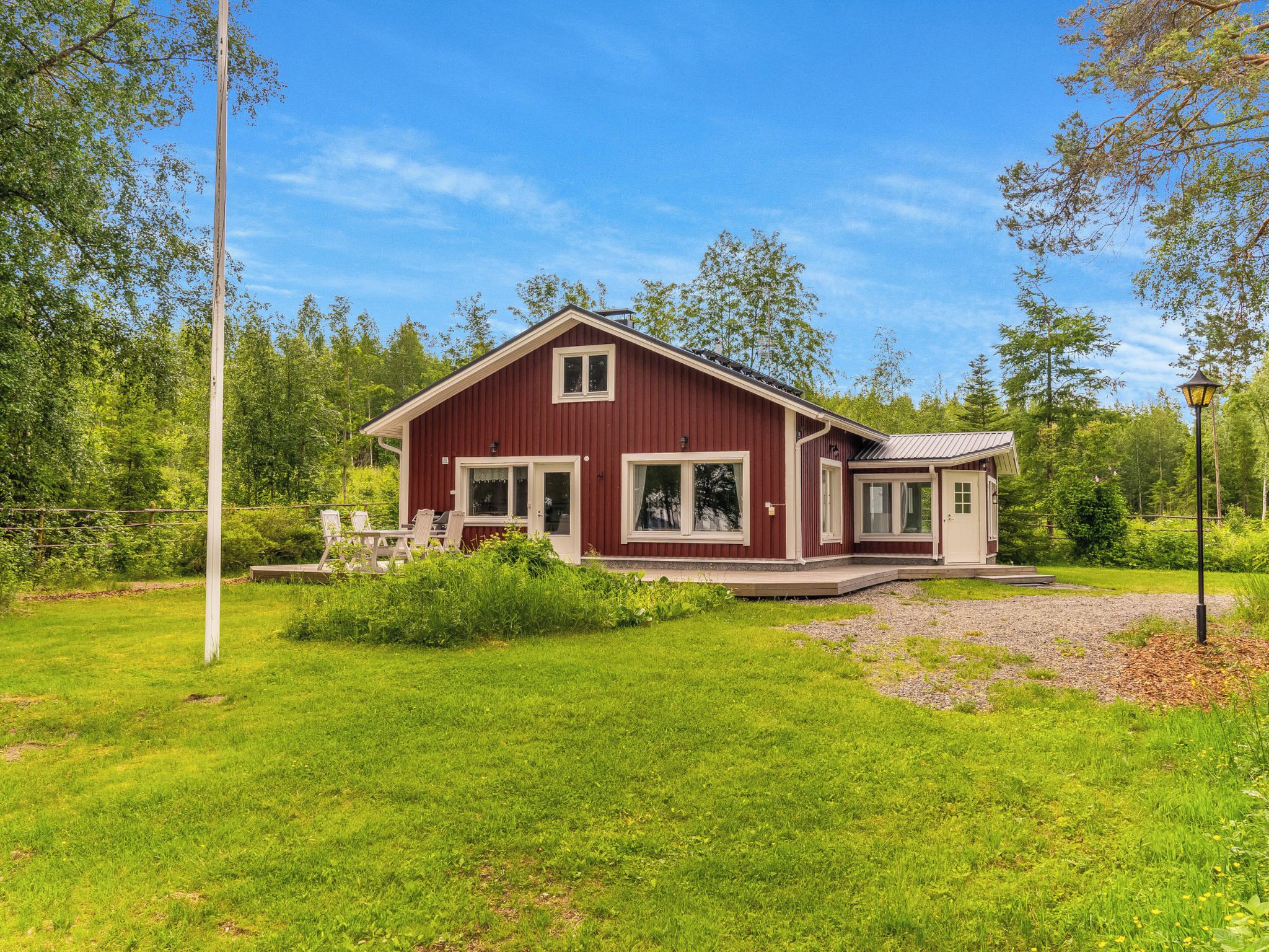 A red wooden house with a porch and a small deck, surrounded by a grassy yard and trees.