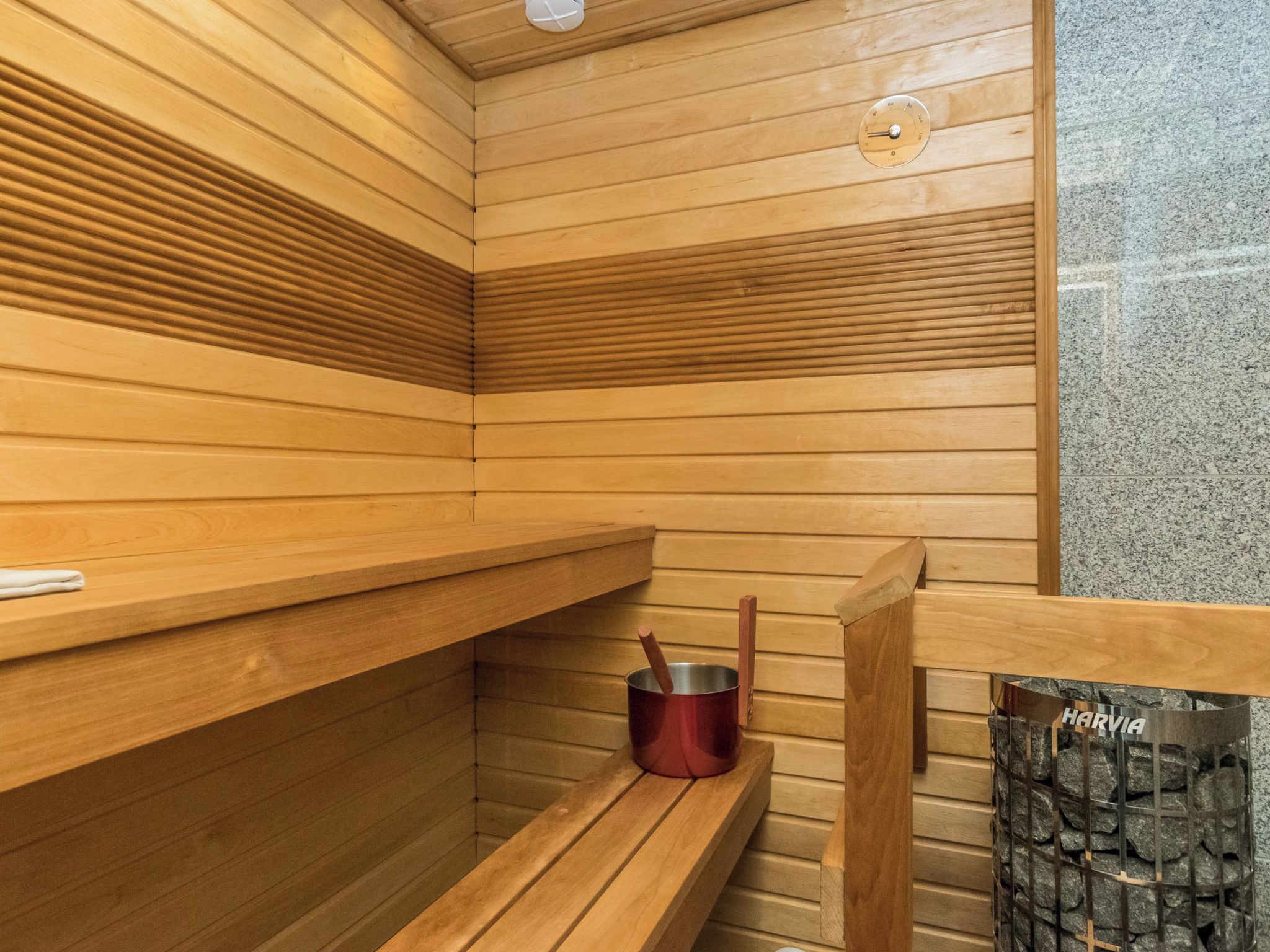 Sauna, jossa on puiset lauteet, metallinen astia ja kiviseinä.