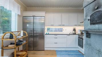 A modern kitchen with white cabinetry, a stainless steel refrigerator, a built-in oven, and a stone fireplace.