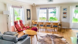 Una habitación con techo de madera, una mesa de comedor con sillas, un sofá, una alfombra y vistas al exterior con vegetación.