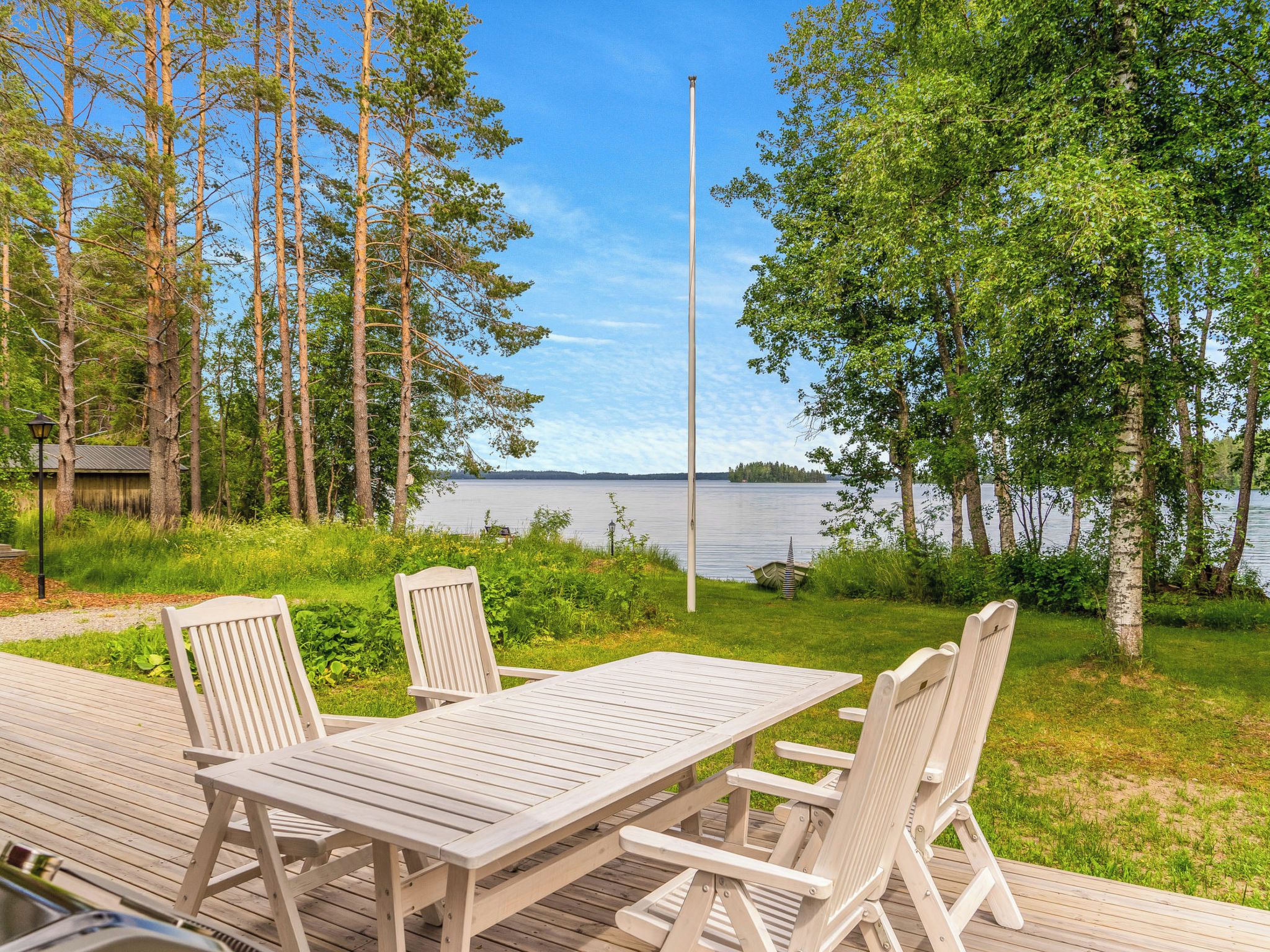 Puisesta laudasta rakennettu terassi, jossa on pöytä ja tuoleja. Terassilta avautuu näkymä järvelle, ja se on ympäröity puilla.