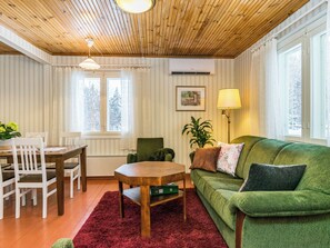 Un salon chaleureux avec un plafond en bois, un canapé vert, une table à manger avec des chaises et un tapis rouge.