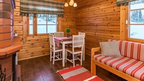 Interior acogedor de una cabaña con detalles de madera, una zona de comedor con mesa y sillas, un sofá con cojines a rayas y una chimenea.