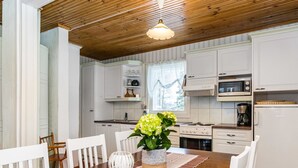 Una cocina moderna con armarios blancos, techo de madera y un comedor con camino de mesa a rayas y sillas blancas.