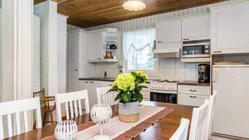 A modern kitchen with white cabinetry, a wooden dining table with chairs, and a hanging light fixture.