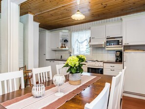 Une cuisine moderne avec des meubles blancs, une table à manger en bois et des chaises, ainsi qu’un luminaire suspendu.