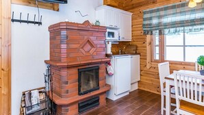 Interior acogedor de una cabaña con chimenea de ladrillo, muebles blancos y una zona de comedor con mesa y sillas.