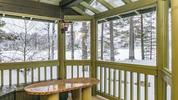 A covered outdoor area with a wooden bench, a view of a snowy forest, and a metal railing.