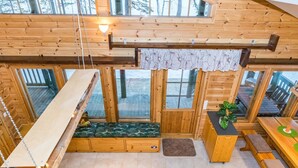 Ein Holzblockbau-Innenraum mit Schlafkoje, einer Couch, einem Esstisch und großen Fenstern.