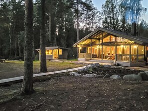 A lodge with a large deck and multiple rooms, surrounded by a forest.