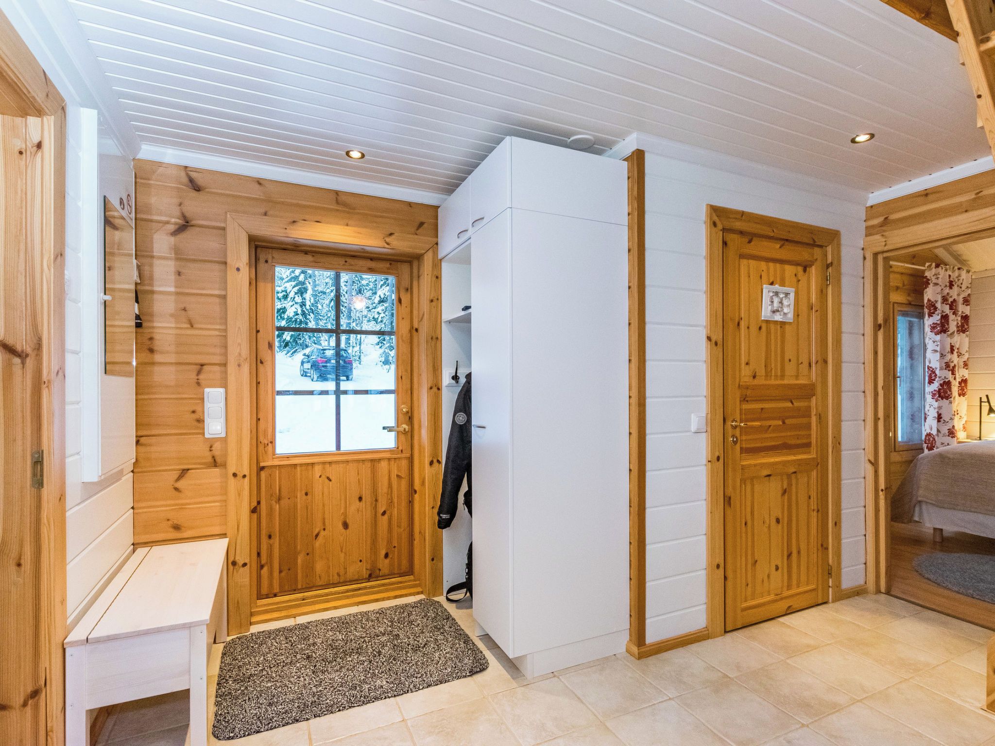 Interior de madera con un banco, una puerta con un número y vistas a un paisaje nevado a través de una ventana.