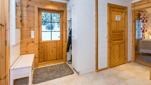 Ein Holzinnenraum mit einer Bank, einer Tür mit Blick, einer weißen Wand und einem Bett mit floralem Vorhang.